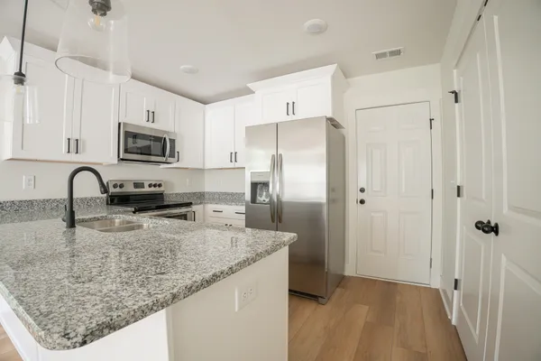 a kitchen with granite countertop a refrigerator a stove a sink a washer and dishwasher with wooden floor