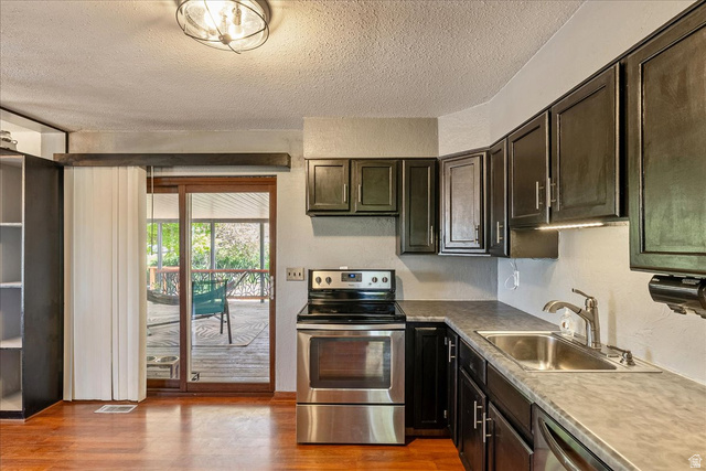 11 South Clark Lane Elk Ridge, UT 84651 - Photo 12 of 46 Kitchen with stainless steel appliances, a textured ceiling, dark wood finish cabinets, light wood-style floors, and light countertops