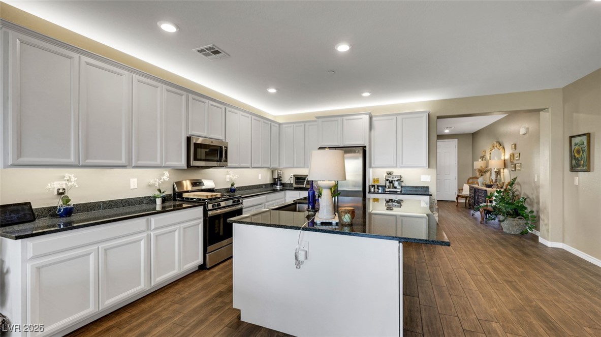 1094 Langston Ranch Avenue Henderson, NV 89002 - Photo 21 of 70 Kitchen featuring appliances with stainless steel finishes, dark stone countertops, a kitchen island, dark wood finished floors, and recessed lighting