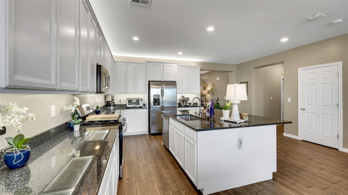 1094 Langston Ranch Avenue Henderson, NV 89002 - Photo 22 of 70 Kitchen with appliances with stainless steel finishes, dark stone counters, recessed lighting, dark wood-style floors, and a center island with sink