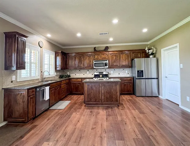 a kitchen with kitchen island granite countertop wooden floors stainless steel appliances a sink and a window