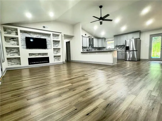 a kitchen with stainless steel appliances granite countertop a refrigerator a sink dishwasher a stove and a dining table with wooden floor