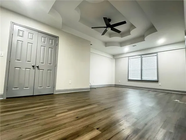 an empty room with wooden floor chandelier fan and windows