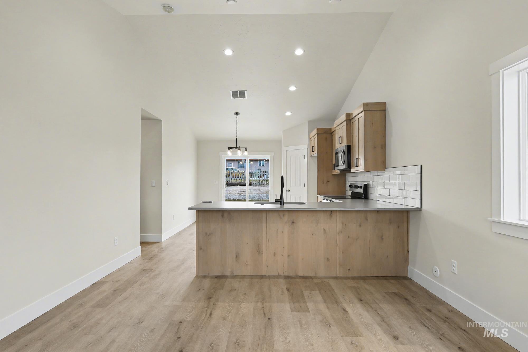 326 Packer Lane Homedale, ID 83628 - Photo 3 of 24 Kitchen featuring vaulted ceiling, tasteful backsplash, hanging light fixtures, light countertops, and a peninsula