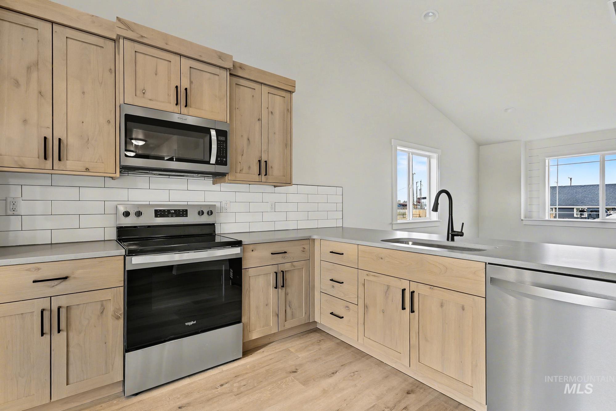 326 Packer Lane Homedale, ID 83628 - Photo 10 of 24 Kitchen with appliances with stainless steel finishes, light brown cabinetry, lofted ceiling, decorative backsplash, and light wood-style floors