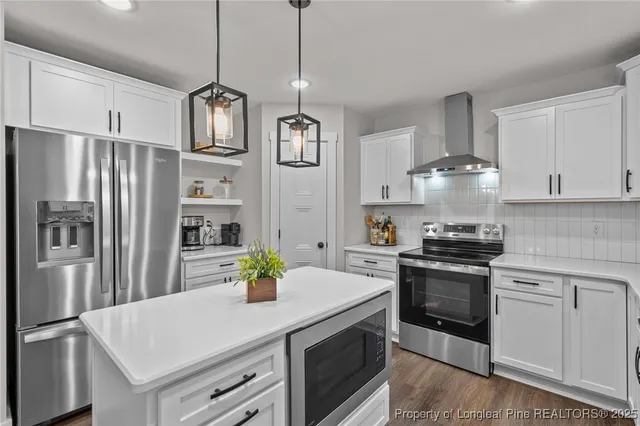 a kitchen with stainless steel appliances granite countertop a sink a stove a refrigerator and a refrigerator with white cabinets