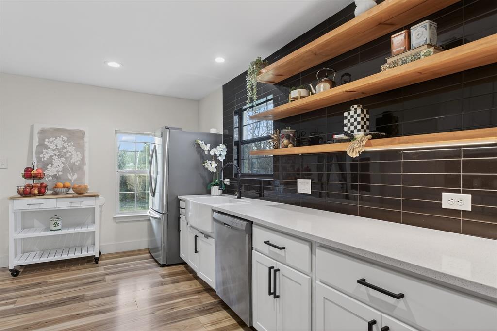 316 Old Justin Road Argyle, TX 76226 - Photo 11 of 40 Show-stopping kitchen with farmhouse sink sits beneath a window overlooking backyard panoramic views & features custom wood shelves, quartz, subway tile backsplash, gorgeous cabinetry, pot filler, 2 large pantries & mudroom.