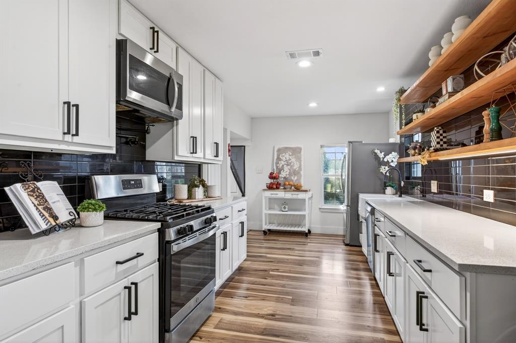 316 Old Justin Road Argyle, TX 76226 - Photo 12 of 40 Show-stopping kitchen with farmhouse sink sits beneath a window overlooking backyard panoramic views & features custom wood shelves, quartz, subway tile backsplash, gorgeous cabinetry, pot filler, 2 large pantries & mudroom.