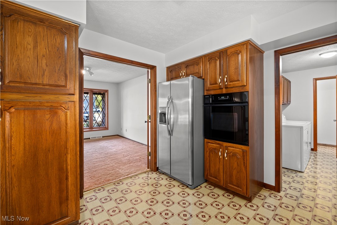 1711 Gulf Road Elyria, OH 44035 - Photo 16 of 50 Kitchen with a textured ceiling, oven, stainless steel refrigerator with ice dispenser, washer / clothes dryer, and brown cabinetry