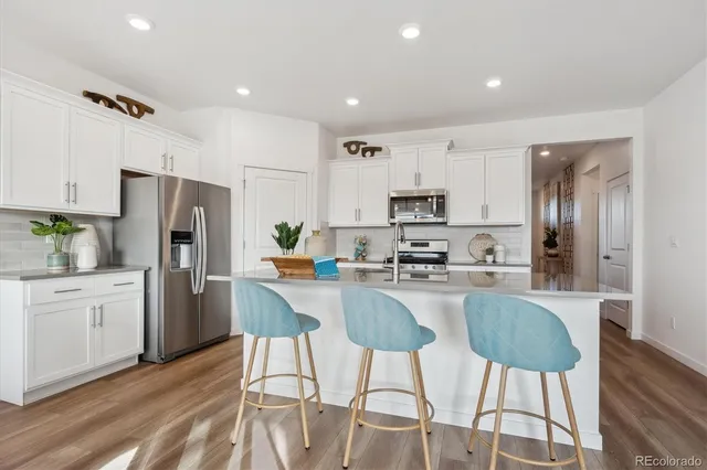 a kitchen with stainless steel appliances a refrigerator a stove a sink a dining table and chairs with wooden floor