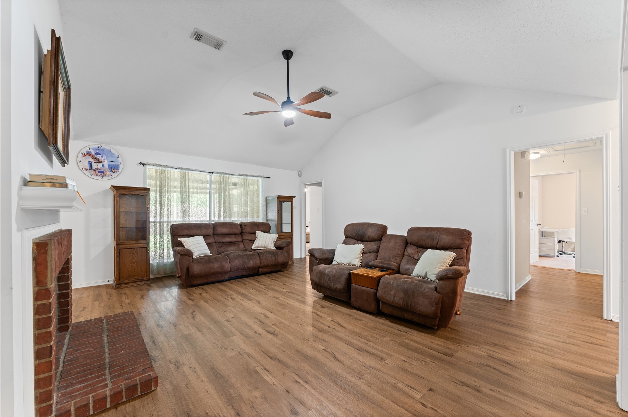 17618 Mill Springs Drive Spring, TX 77379 - Photo 11 of 26 Spacious living room with high ceilings, laminate flooring, and a cozy brick fireplace. Features comfortable seating, natural light from large windows, and a ceiling fan for airflow.