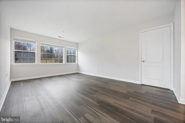 a view of an empty room with wooden floor and windows