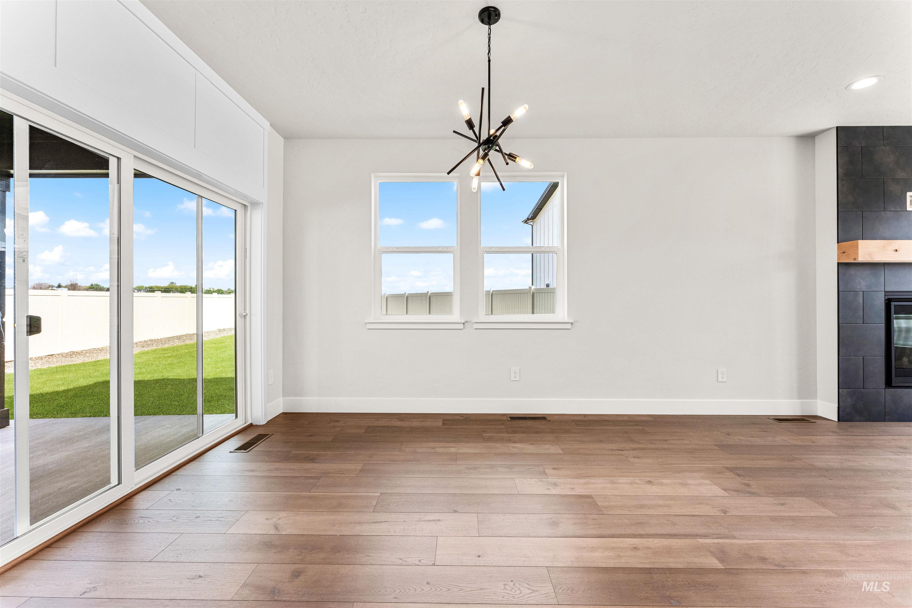 2709 West Gidran Meridian, ID 83642 - Photo 11 of 43 Spacious room featuring wood-finish flooring, a contemporary black chandelier, and a built-in fireplace with a dark tile surround and a natural wood mantel