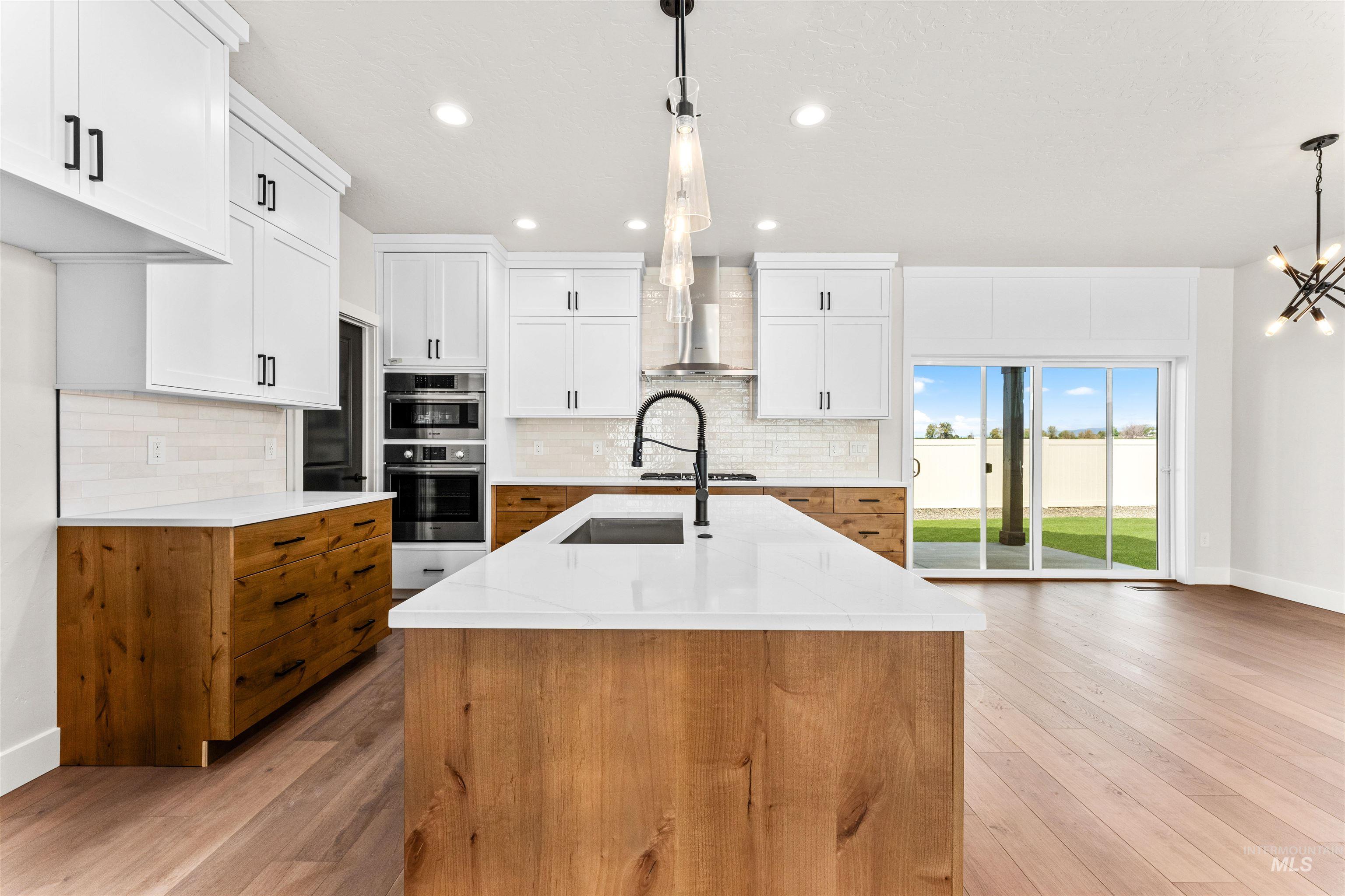 2709 West Gidran Meridian, ID 83642 - Photo 14 of 43 Modern kitchen featuring a large central island with a built-in sink, white countertops, and wood-finish cabinetry