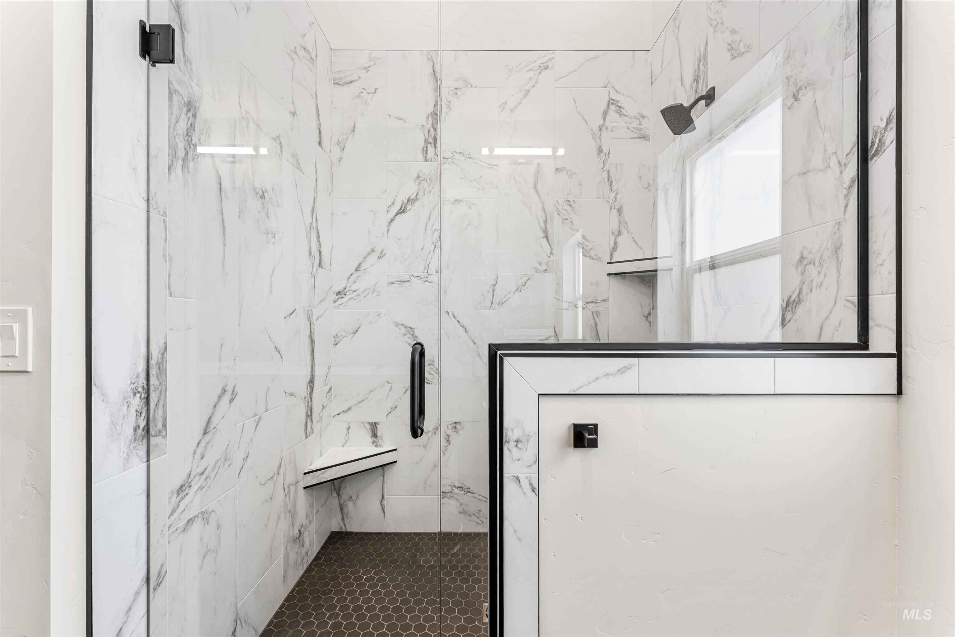 2709 West Gidran Meridian, ID 83642 - Photo 24 of 43 Walk-in shower featuring a frameless glass enclosure with matte black hardware, white marbled tile walls, a built-in shower bench, a recessed shower niche, and hexagonal floor tiling
