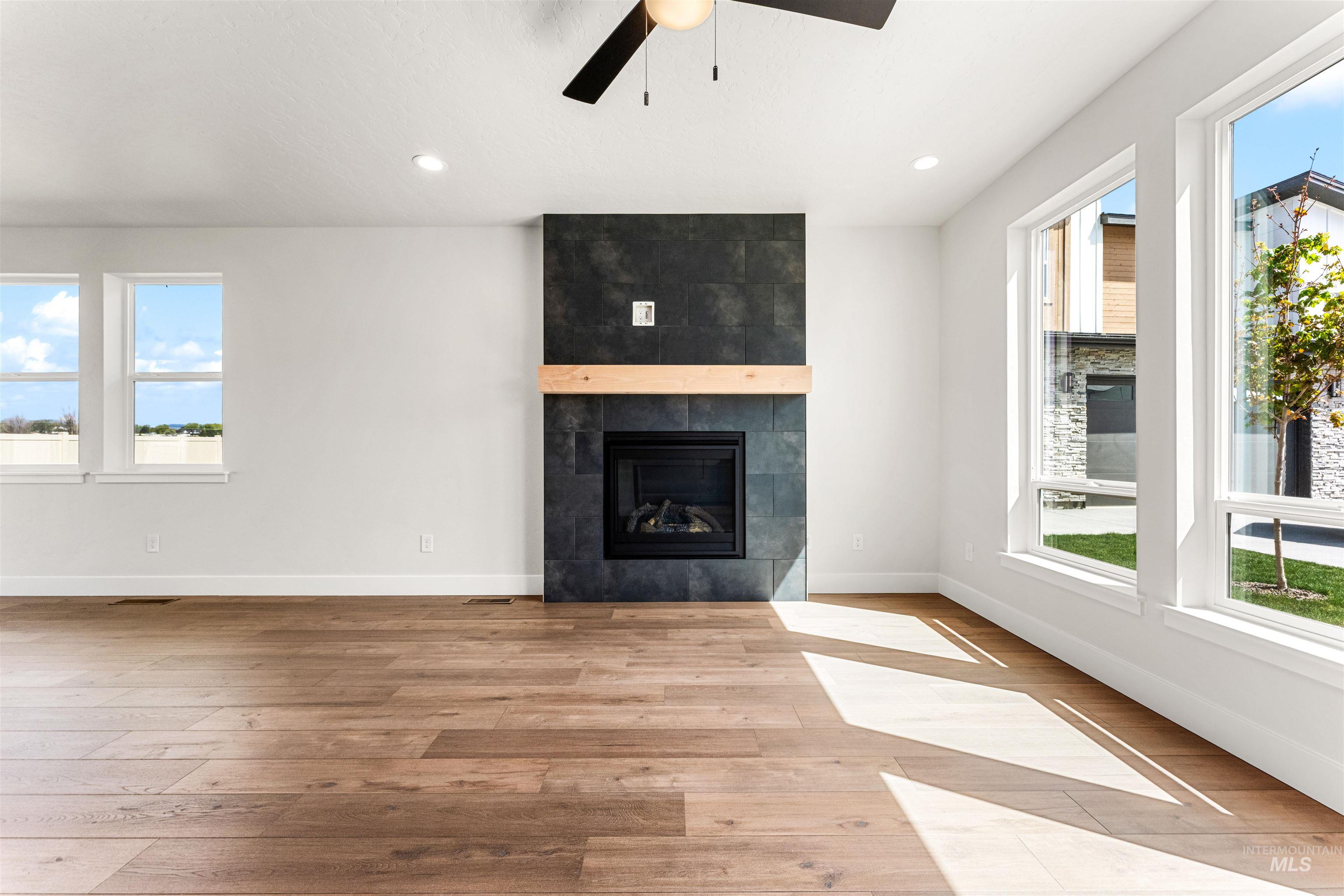 2709 West Gidran Meridian, ID 83642 - Photo 3 of 43 Spacious interior featuring wood-finish flooring, a contemporary fireplace with dark tile surround and wood mantel, white walls, and multiple windows