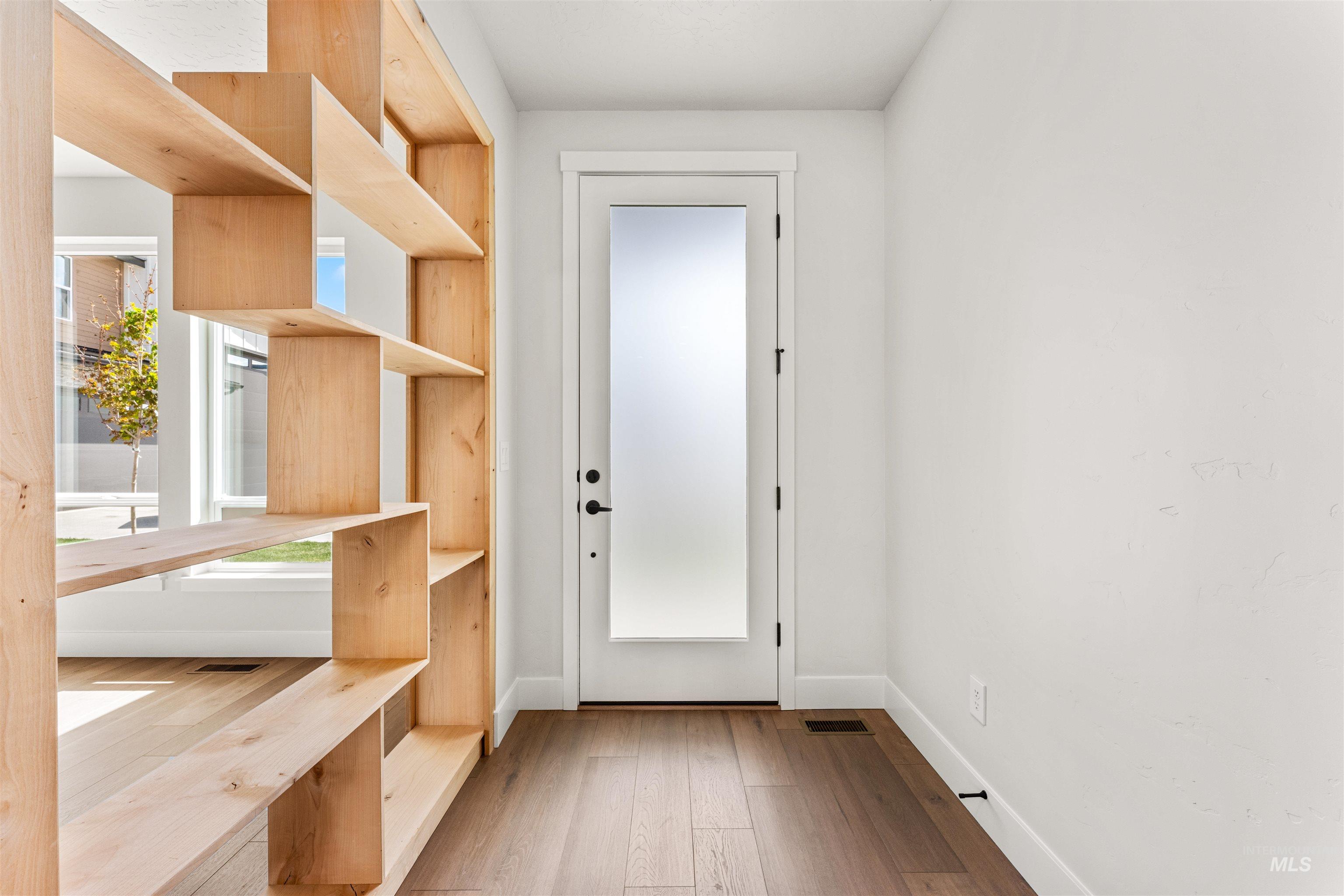 2709 West Gidran Meridian, ID 83642 - Photo 4 of 43 Open-concept living space featuring a custom wood shelving unit, wide plank wood-finish flooring, white walls, and a frosted glass panel door