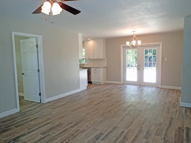 an empty room with wooden floor chandelier and windows
