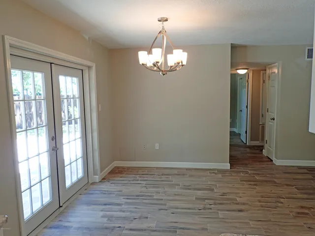 a view of a chandelier in big room with wooden floor and windows