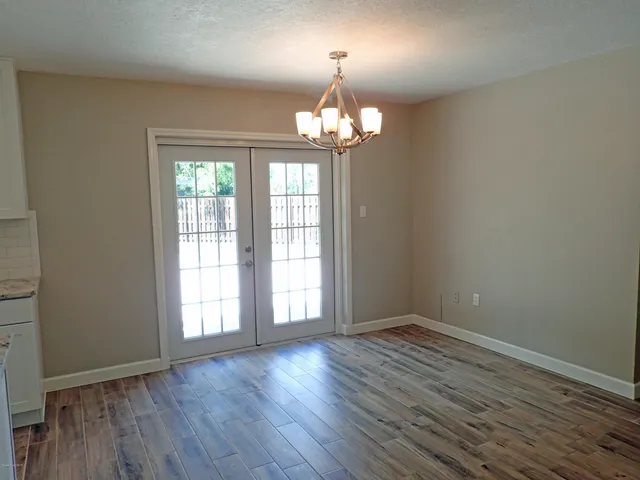 an empty room with wooden floor chandelier and windows