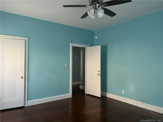 an empty room with wooden floor closet ceiling fan and windows
