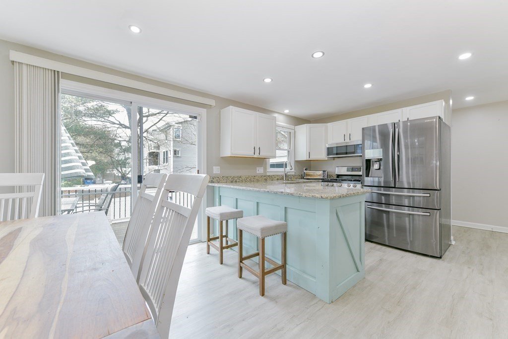 a kitchen with stainless steel appliances granite countertop a refrigerator a sink dishwasher a stove and a dining table with wooden floor