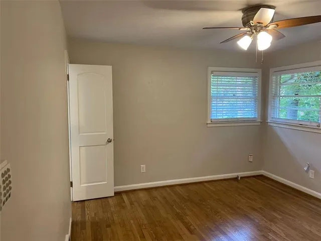 an empty room with wooden floor fan and windows