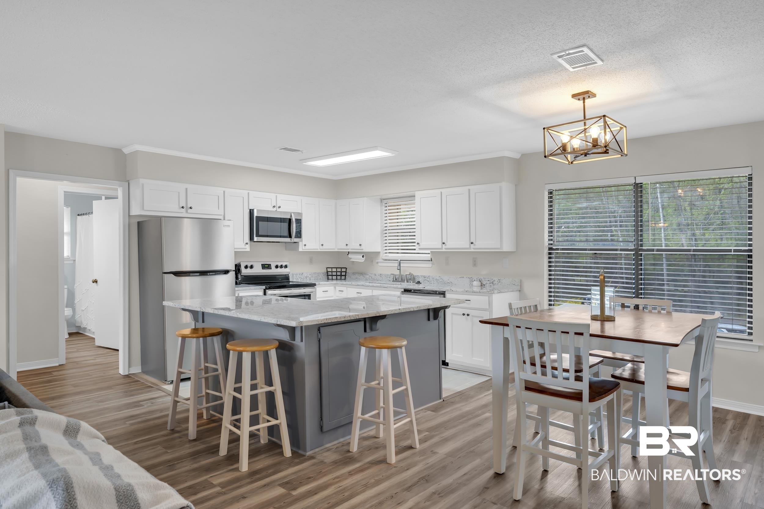 8081 Bryant's Lndg Road Stockton, AL 36579 - Photo 26 of 48 Two tone kitchen featuring light stone counters, stainless steel appliances, a center island, a kitchen breakfast bar, and light wood-type flooring