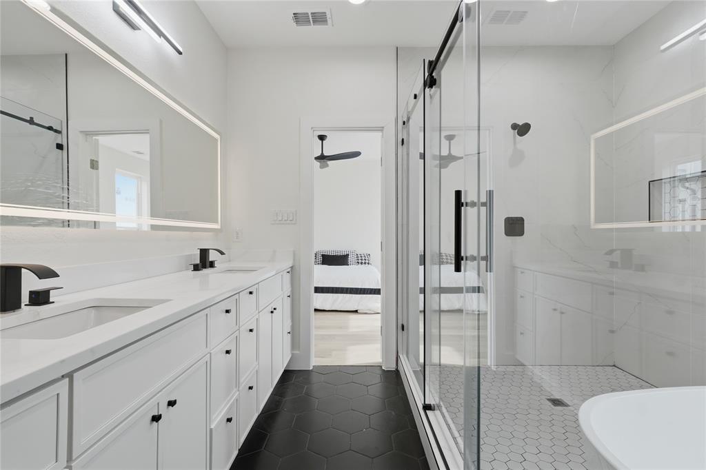 3905 Blue Ridge Boulevard Dallas, TX 75233 - Photo 17 of 25 Dual vanity with integrated sinks, back-lit mirrors, matte black fixtures, frameless glass shower enclosure, and hexagon tile flooring