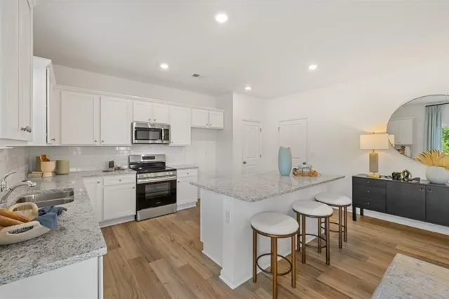 a kitchen with stainless steel appliances granite countertop a stove top oven a sink dishwasher and white cabinets with wooden floor