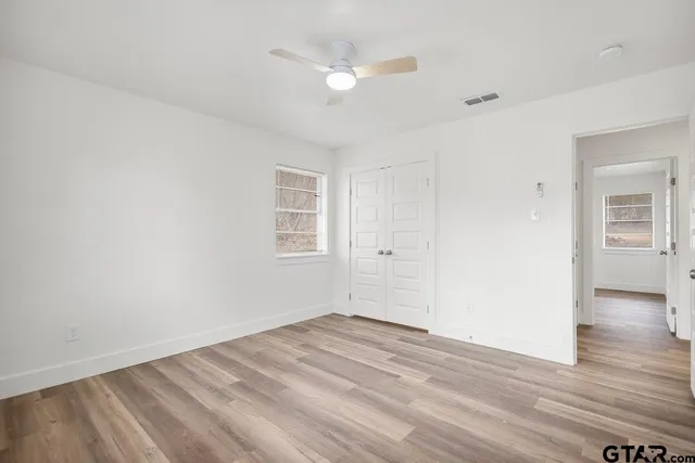 an empty room with wooden floor ceiling fan and windows