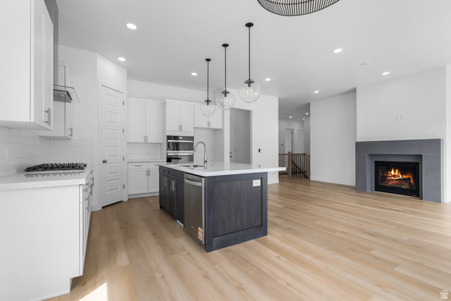 43 South Crimson Way, Unit 311 Mapleton, UT 84664 - Photo 5 of 28 Contemporary kitchen featuring a dark gray island with a sink and pendant lighting, white cabinetry, a built-in oven, and a gas cooktop with a tiled backsplash