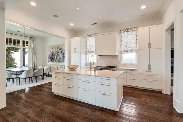 a kitchen with stainless steel appliances granite countertop a stove a sink and white cabinets with wooden floor next to windows