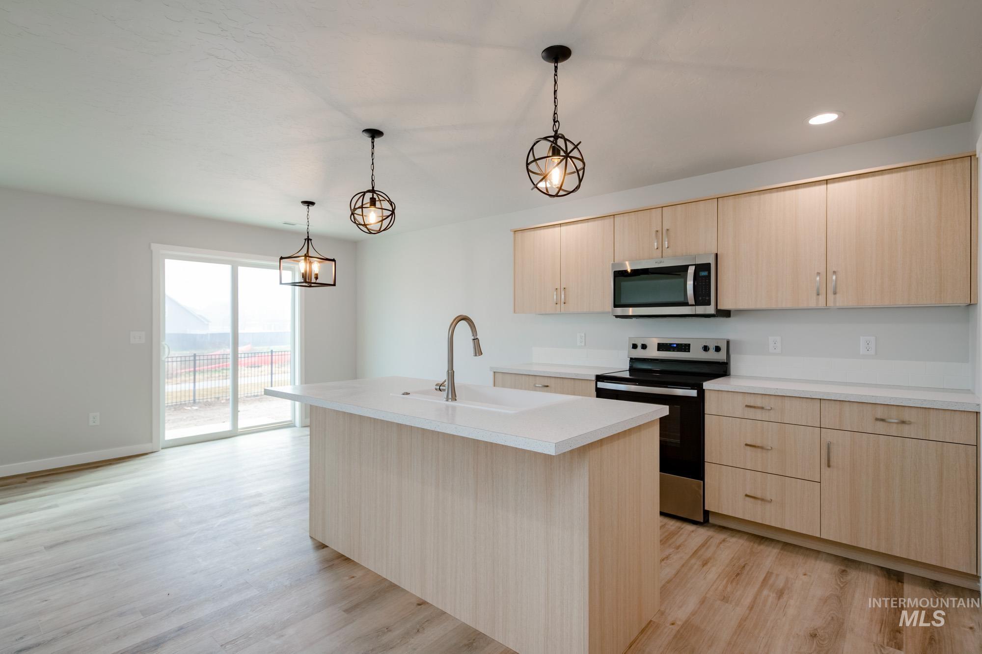 2486 West Fallon Loop Nampa, ID 83651 - Photo 4 of 18 Kitchen featuring stainless steel appliances, light countertops, a kitchen island with sink, light brown cabinets, and hanging light fixtures