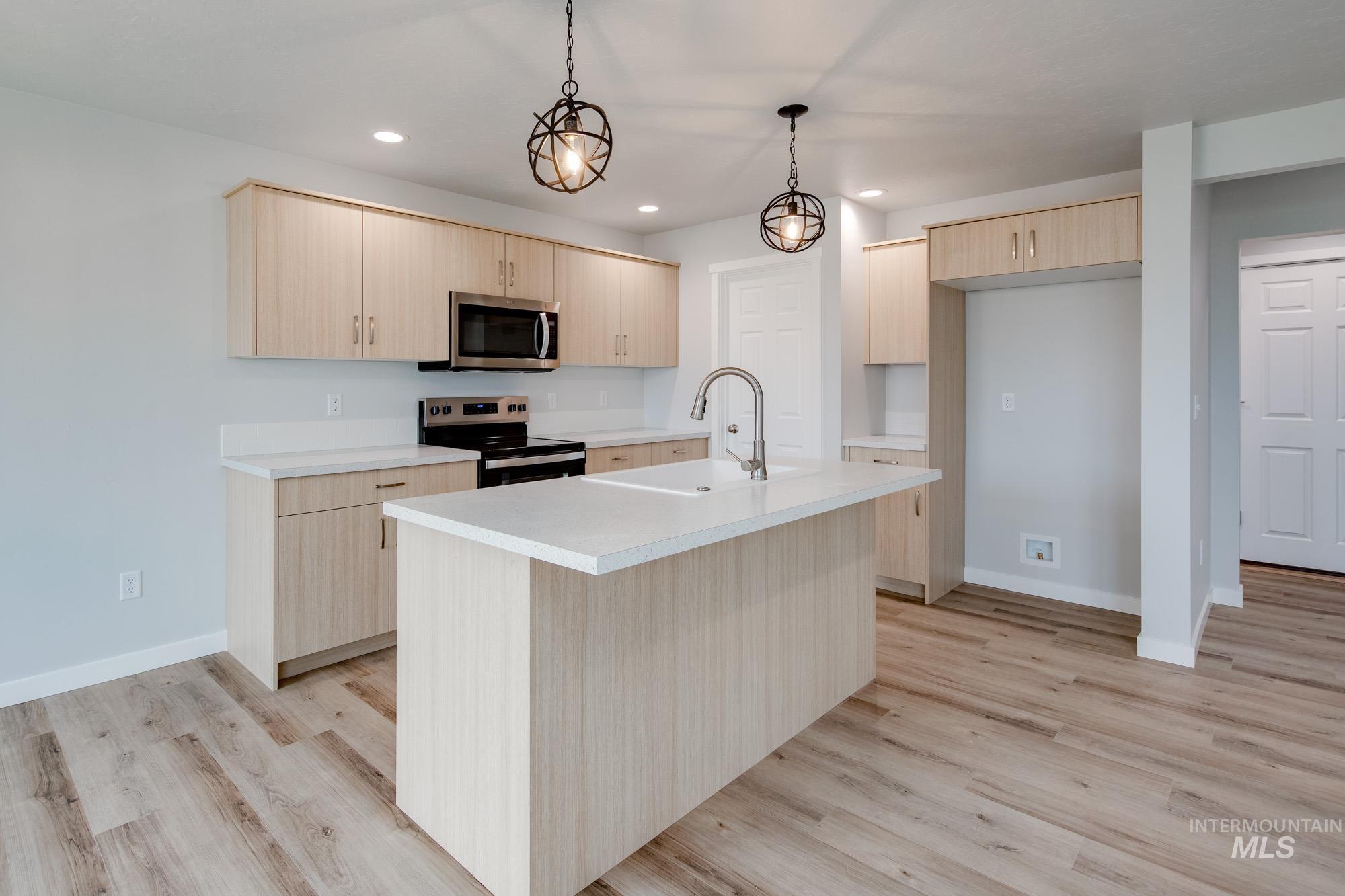 2486 West Fallon Loop Nampa, ID 83651 - Photo 7 of 18 Kitchen with light brown cabinetry, light countertops, appliances with stainless steel finishes, pendant lighting, and light wood finished floors