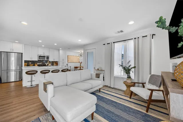 a living room with couches kitchen view and a large window