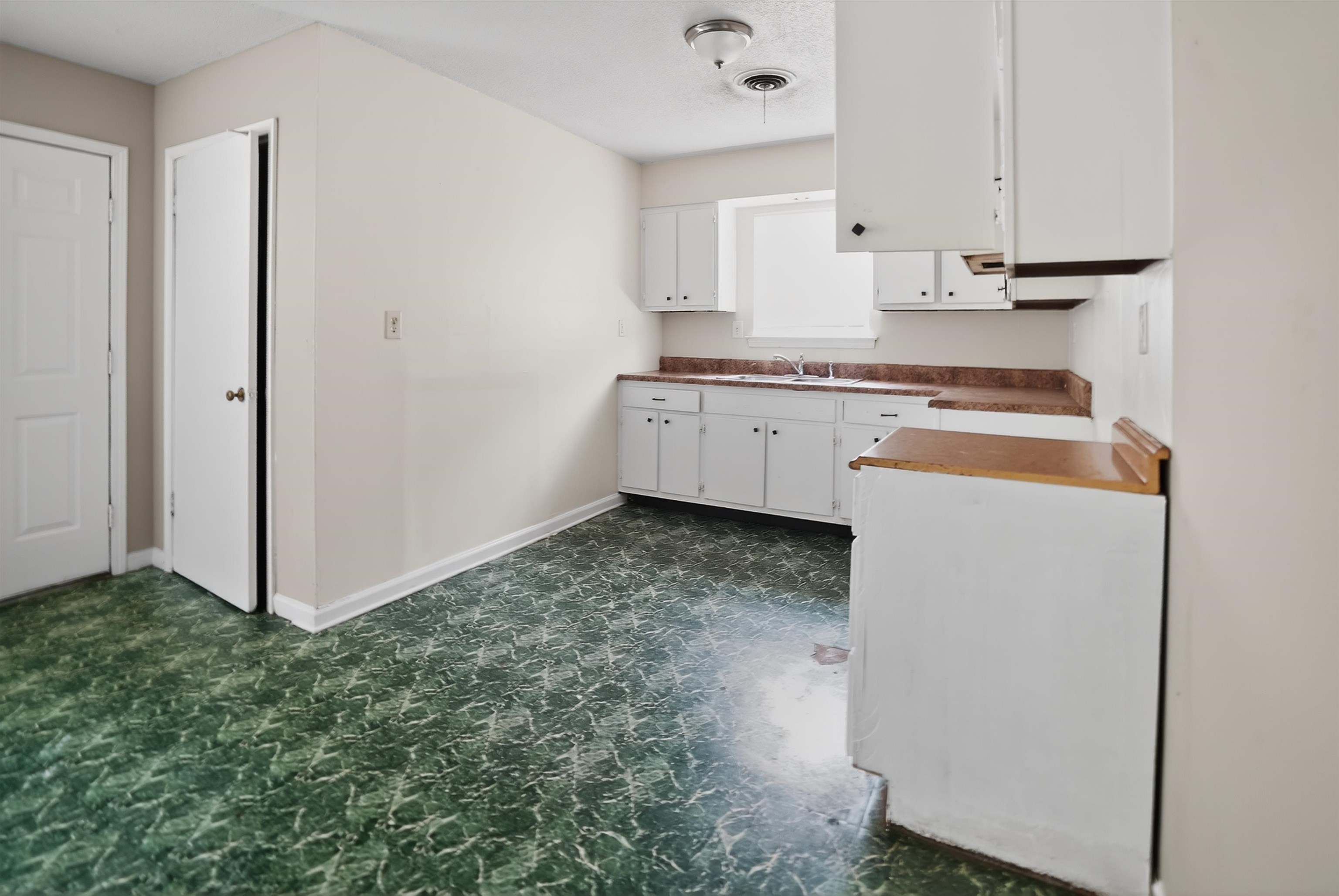 4530 Spring Valley Drive Memphis, TN 38128 - Photo 10 of 15 Kitchen featuring white cabinetry, a built-in sink under a window, wood-finish countertops, and patterned green flooring
