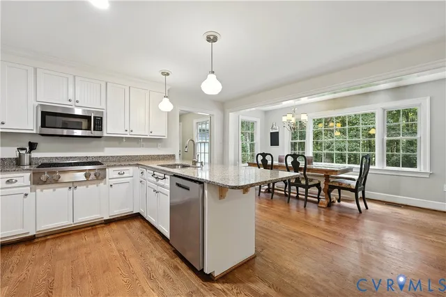 a kitchen with stainless steel appliances granite countertop a stove top oven a sink a dining table and chairs with wooden floor