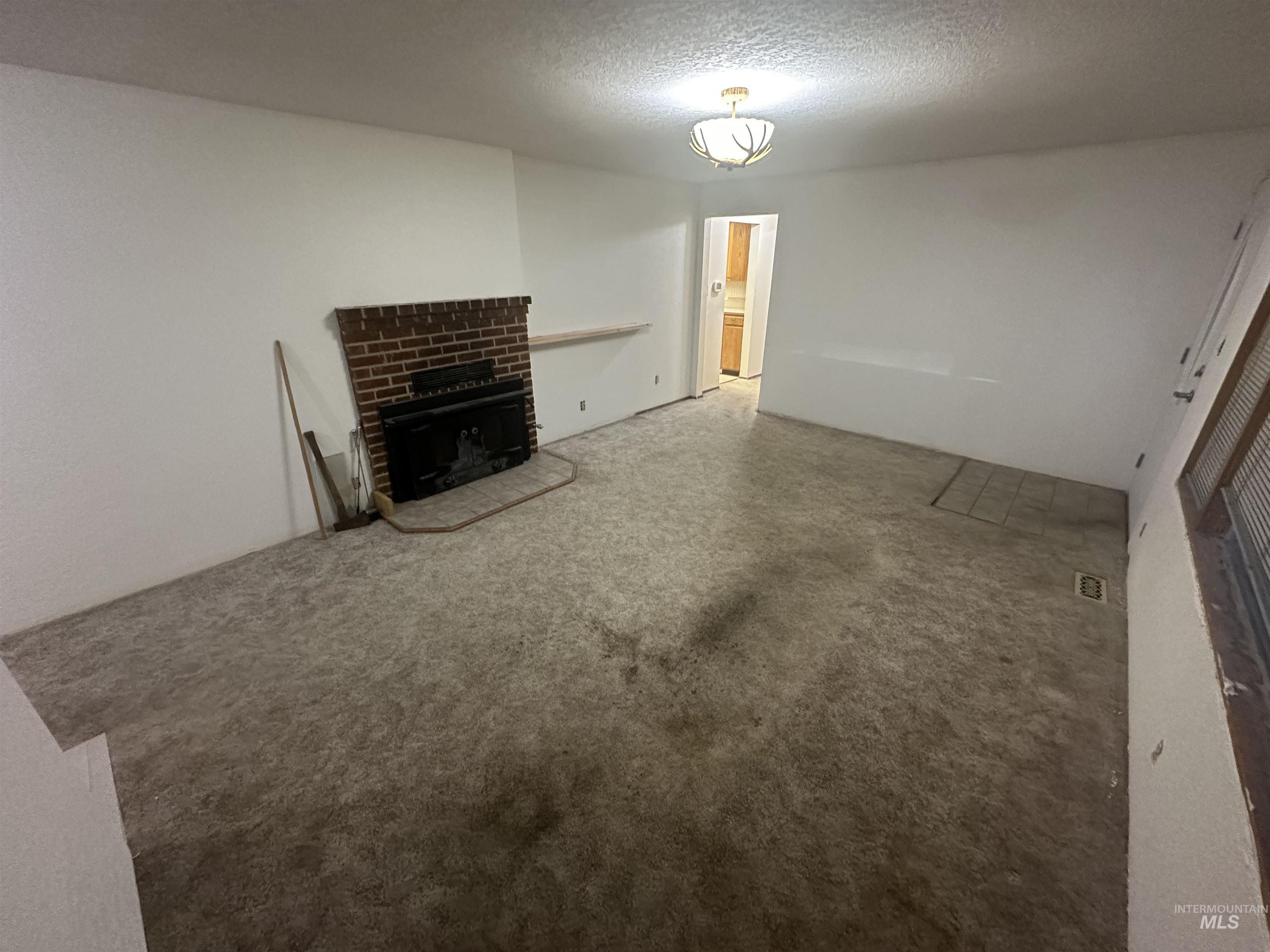 410 South Yakima Street Vale, OR 97918 - Photo 9 of 29 Unfurnished living room featuring a fireplace, a textured ceiling, and carpet floors