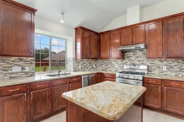 a kitchen with stainless steel appliances granite countertop wooden cabinets a sink and dishwasher a stove top oven with wooden floor