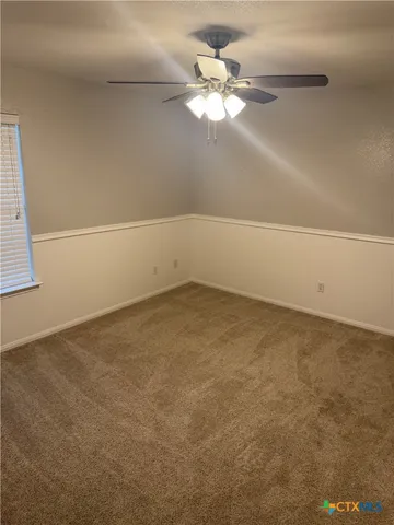 an empty room with a chandelier fan and windows
