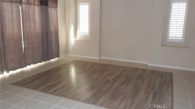 an empty room with wooden floor and windows with curtains