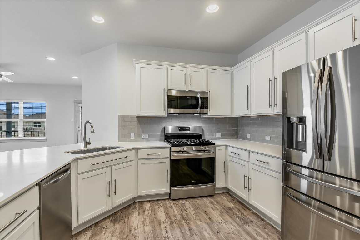 5125 Vanner Path Georgetown, TX 78626 - Photo 12 of 27 Kitchen featuring stainless steel appliances, white cabinets, recessed lighting, light wood-style flooring, and tasteful backsplash