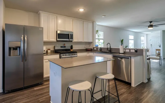 a kitchen with stainless steel appliances granite countertop a sink a stove a refrigerator cabinets and a dining table with wooden floor