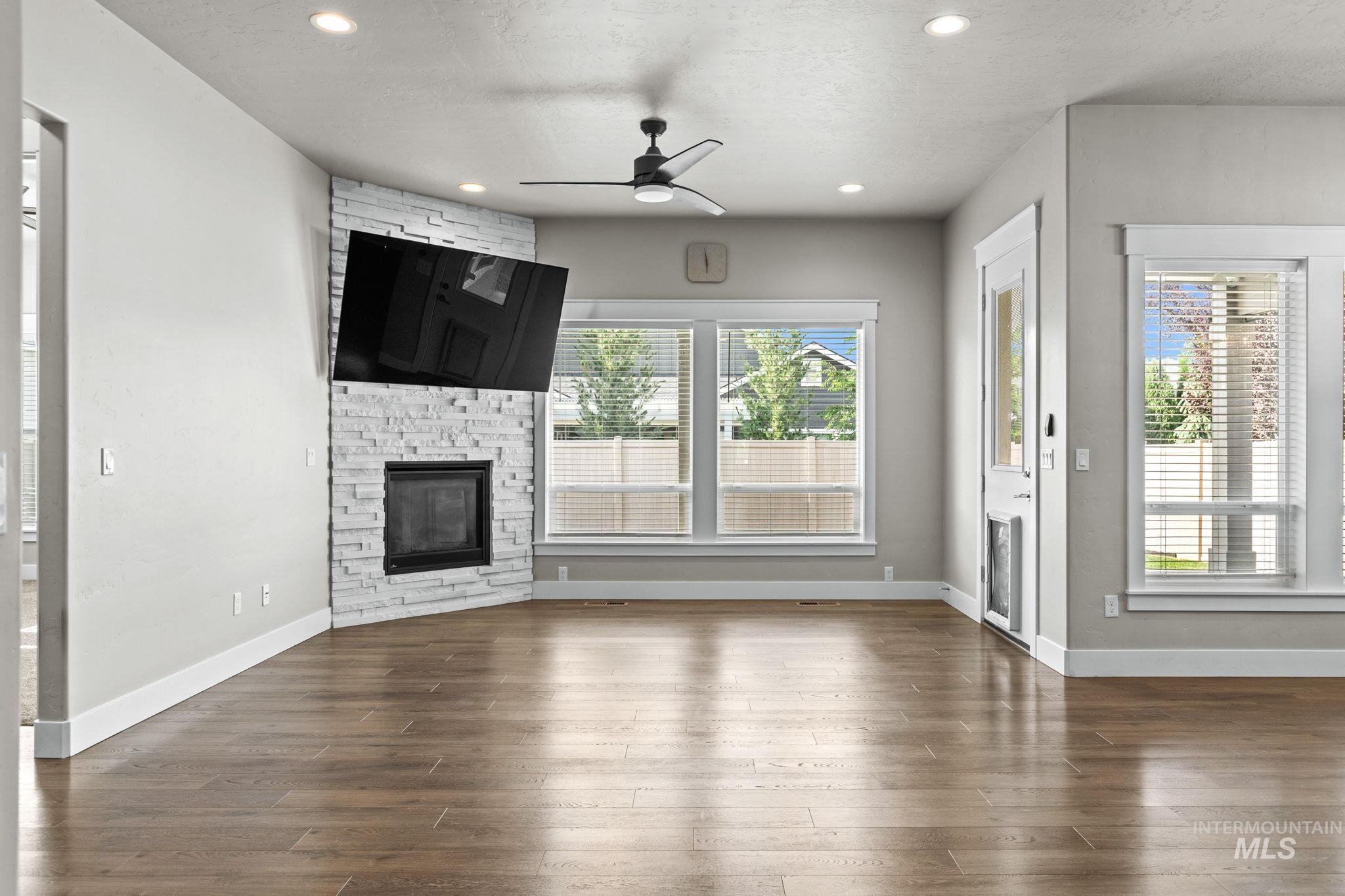 2934 East Murchison Street Meridian, ID 83642 - Photo 16 of 44 Spacious living area featuring wood-finish flooring, a corner fireplace with stacked stone surround, and multiple windows with blinds
