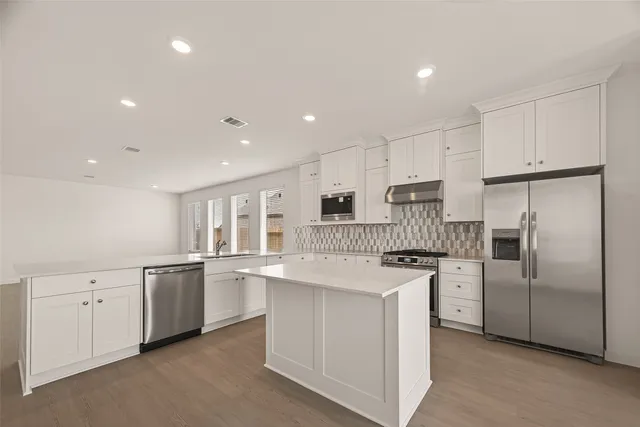 a kitchen that has a lot of white cabinets and stainless steel appliances