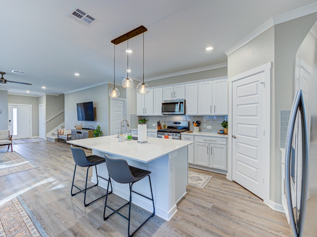 a kitchen with stainless steel appliances kitchen island granite countertop a refrigerator a stove top oven a sink dishwasher and white cabinets with wooden floor