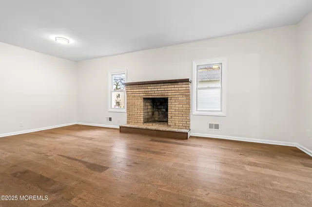 an empty room with wooden floor fireplace and windows
