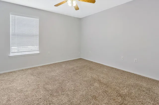 an empty room with a ceiling fan and carpet