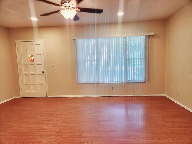 an empty room with wooden floor chandelier fan and windows